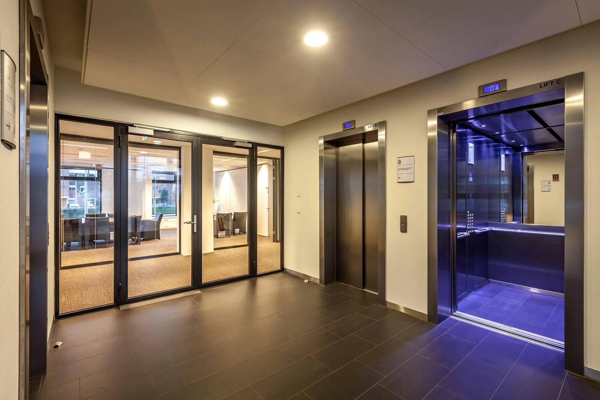 Moderne liftlobby met drie liften en glazen deuren naar een kantoorruimte aan de Prinses Beatrixlaan.